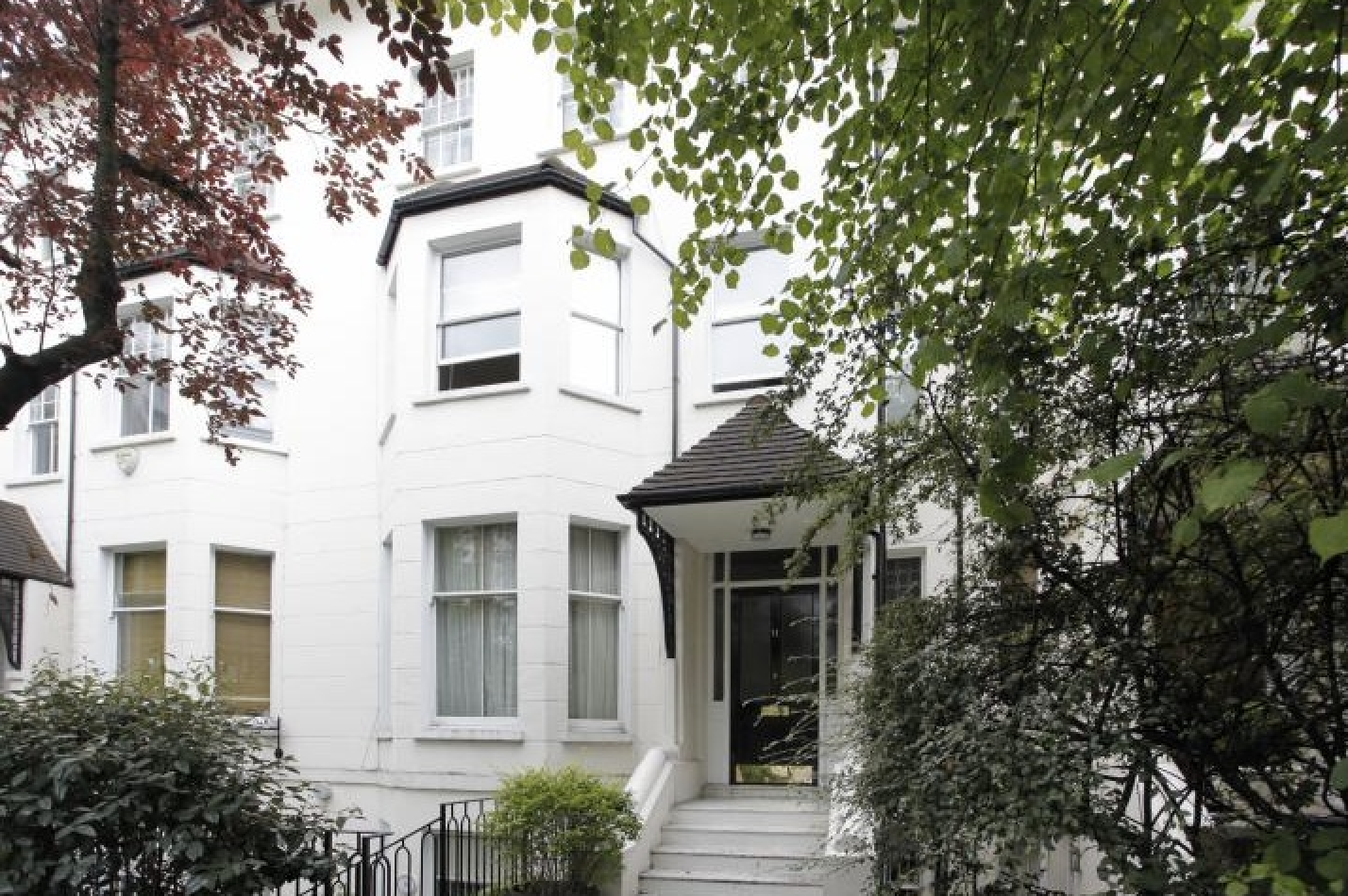 Front exterior of the white-painted Victorian villa on Abbey Road, St John's Wood NW8 — pillared entrance porch, bay windows, framed by mature trees.